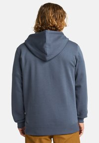 Hætte sweatshirt i mørkeblå stof med ribbede manchetter og kant. Bagfra ses en glat overflade og et enkelt design uden mønstre eller accenter.