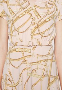 Vestido rosa claro con intrincados patrones de arneses dorados, mangas cortas, un cierre frontal abotonado y una cintura ceñida con un cinturón con hebilla redonda.