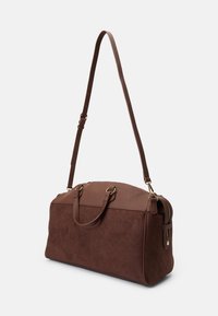 Brun duffelbag som kombinerer glatte og teksturerte materialer, med justerbar skulderreim, doble toppløkker og detaljer i gulltone.