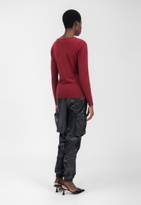 Maglione rosso lavorato a maglia, design aderente, maniche lunghe, abbinato a pantaloni cargo neri in ecopelle con tasche laterali e scarpe nere con tacco.