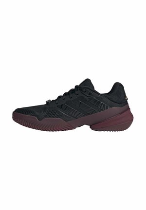 Schwarzer Low-Top-Athletikschuh mit strukturiertem Obermaterial, Schnürverschluss und dicker weinroter Sohle, isoliert auf weißem Hintergrund.