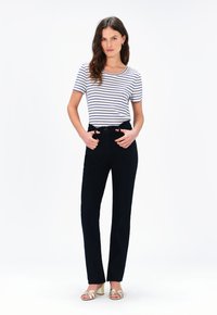 Gestreepte t-shirt met korte mouwen in grijs en marineblauw, gecombineerd met hoog getailleerde zwarte jeans. Model staat met handen in de zakken en draagt metalen hakken.