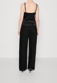 Svart satin camisole med tunna remmar, kombinerad med vida svarta byxor som har en diskret textur och spridda utsmyckningar.
