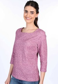 Enganliegendes Oberteil aus helllila Stoff mit Blumenmuster, runder Ausschnitt und dreiviertelärmel, kombiniert mit blauen Jeans.