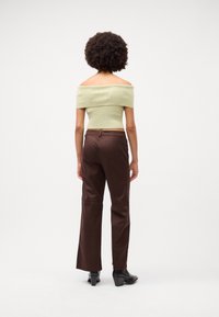 Top s odhalenými rameny, žebrovaný světle zelený crop top, spárovaný s hnědými, vysokými kalhotami s rovnými nohavicemi a černými koženými kotníkovými botami na podpatku.