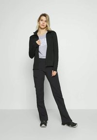 Svart zip-up jakke over en grå t-skjorte, paret med svarte bukser og svart fottøy. Enkelt design, tettsittende silhuett.