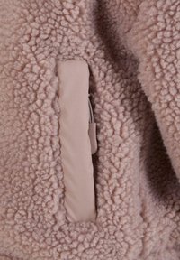 Lett, lyserosa fleece med en myk, teksturert overflate og en skjult lomme i lys beige stoff. Enkel og funksjonell design.