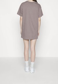 T-shirt oversize in malva realizzata in tessuto morbido, con maniche corte e orlo arrotondato, abbinata a sneaker bianche e calzini chiari.