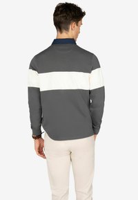 Camicia a maniche lunghe con corpo grigio, colletto blu navy e una striscia bianca orizzontale sulla schiena. Realizzata in tessuto testurizzato, ha una vestibilità casual.