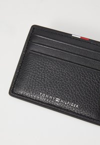 Black leather cardholder with multiple slots and a textured finish. Features embossed "TOMMY HILFIGER" logo at the base.