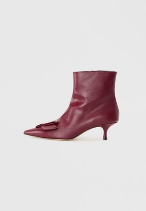 Bottino in pelle bordeaux con punta affusolata, dotato di una fibbia decorativa, una silhouette slanciata e un tacco kitten basso.
