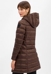 Bruine gewatteerde jas met capuchon, met een gestikte ontwerp, zwarte logo patch op de schouder en een gladde, glanzende textuur.