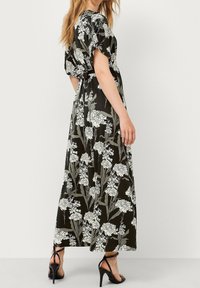 Maxi kjole i sort stof med hvidt blomstermønster. Korte ærmer, løs pasform, bælte i taljen. Bæres med sorte strop sandaler.