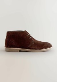 Stivaletto in suede marrone con punta arrotondata, design con lacci a due fori, suola in gomma beige e dettagli con cuciture a contrasto.