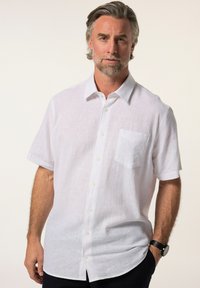Camicia bianca in lino a maniche corte con tasca, chiusura frontale a bottoni e vestibilità rilassata. Texture liscia con un aspetto leggero.