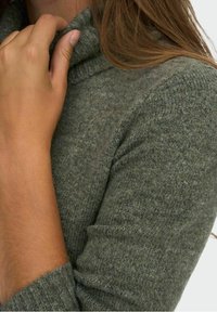 Pull col roulé vert olive en tissu tricoté texturé, avec des manches longues et une coupe ajustée au niveau du col et des poignets.