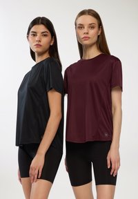 Czarne i burgundowe koszulki sportowe z krótkim rękawem, o gładkiej fakturze i szwach na ramionach. Zestawione z czarnymi szortami.