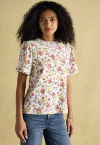 Bluzka w kwiatowy nadruk z krótkimi bufkami, okrągłym dekoltem i koronkowym wykończeniem, wykonana z lekkiego materiału w kremowych, różowych i zielonych odcieniach.