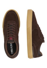 Bruna mockaskon med gummisulor, med grå meshdetaljer, bruna snören och en logotyp nära ankeln. Inuti visar de en dämpad innersula.