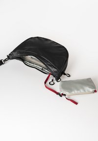 Schwarze Nylon-Tasche mit geschwungenem Design, Reißverschluss und Innentaschen; enthält ein abnehmbares silbernes Täschchen mit rotem Riemen.
