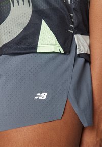 Close-up of a person wearing perforated gray New Balance athletic shorts and a layered, patterned sports top.