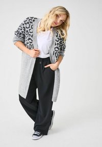 Cárdigan gris con estampado de leopardo negro, de mangas largas, frente abierto, tejido texturizado. Combinado con pantalones negros y zapatillas negras.