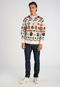 Gebreide feestdagensweater, crème basis, versierd met peperkoekmannetjes, huizen, bomen en sneeuwvlokken in rood, groen en goud. Geribbelde manchetten en onderkant.