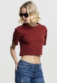 Cropped, short-sleeve t-shirt in deep red cotton fabric. Paired with blue distressed jeans, showcasing a smooth, casual design.