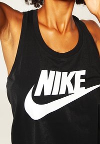 Černý bezrukávový top vyrobený z hladkého materiálu, s výrazným bílým logem Nike na hrudi a kulatým výstřihem.