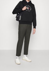 Sudadera negra con logo blanco, pantalones verde oliva y zapatillas blancas. El atuendo incluye un bolso negro de hombro con un acento estampado.