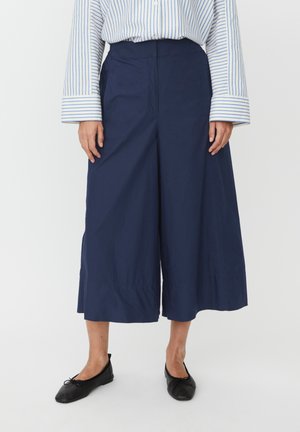 Granatowe spodnie o szerokich nogawkach wykonane z gładkiej, lekkiej tkaniny, z wysokim stanem i krojem culotte. Połączone z czarnymi balerinami.
