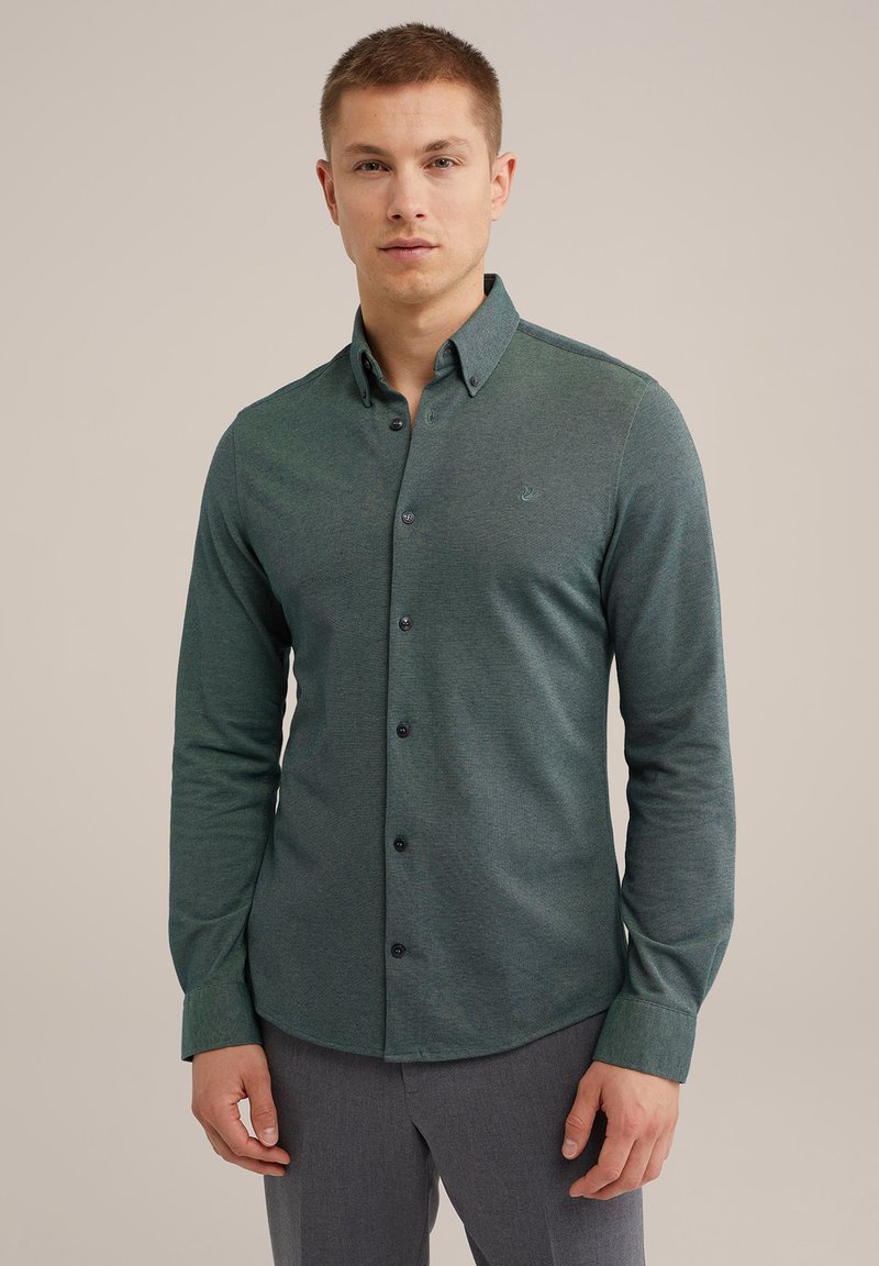 Camisa verde de botón con una textura sutil, mangas largas y collar en punta. Presenta botones oscuros y un pequeño emblema en el pecho.