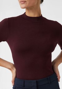 Burgundowy dopasowany sweter z wysokim okrągłym dekoltem i krótkimi rękawami, wykonany z gładkiego materiału o delikatnej fakturze.