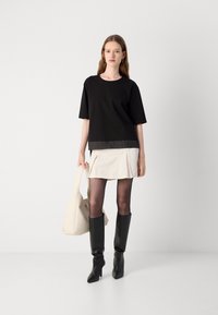 Black short-sleeve top with a contrasting hem, paired with a beige mini skirt, black knee-high boots, and a beige shoulder bag.