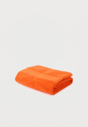 Heldere oranje opgevouwen badhanddoek met een textuurstrookdetail, plat liggend op een wit oppervlak.