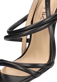 Sandalia de tacón negro con tiras entrelazadas en cuero suave, plantilla beige y un elegante diseño de punta abierta.