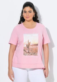 Pink cotton t-shirt med korte ærmer har et ørkenmotiv med en kaktus og teksten "Dage i Sommer." kanten er let buet.