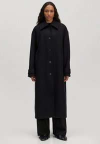 Zwarte wollen jas met een grote kraag, knoopsluiting aan de voorkant en zijzakken. Het ontwerp is lang en oversized met opgerolde manchetten.