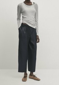 Chemise à manches longues rayée gris clair et noir, associée à un pantalon large bleu marine et des chaussures à lacets brunes. Design simple et texture douce.