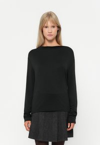 Haut noir à manches longues avec un col large, fabriqué en tissu lisse et léger ; associé à une jupe gris plissée.