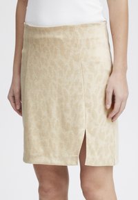Mini jupe à imprimé léopard beige avec une fente sur le côté et une texture lisse. Fabriquée en tissu léger avec un design ajusté pour le confort.