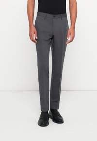 Gray dress pants in a slim fit design, featuring a flat front and side pockets. Worn with black shoes and a fitted black shirt.