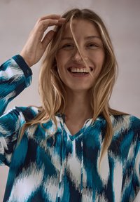 Blusa a maniche lunghe blu e bianca con motivo astratto, dotata di scollo a V, polsini con bottoni e tessuto leggero.