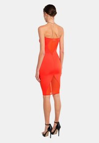 Rotes, trägerloses Kleid mit figurbetontem Oberteil, Ausschnitt auf dem Rücken und knielangem Saum. Getragen mit schwarzen High-Heels.