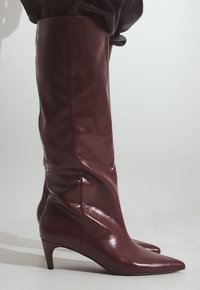 Burgundowe skórzane botki po kolana z eleganckim fasonem, spiczastym noskiem i umiarkowanym obcasem. Gładka faktura i minimalne detale szwów.