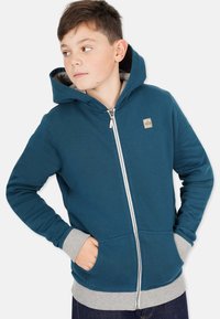 Teal zip-up hoodie med grå insida, framfickor och ribbade muddar. Har en liten logotagg på vänster bröst.