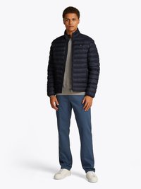 Navy puffer jacket with vertical quilting, gray sweater, light blue pants, and white sneakers. Jacket features a stand collar and zip closure.