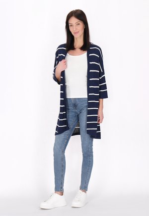 Námořnický cardigan s bílými vertikálními pruhy, středně dlouhými rukávy, otevřený vpředu, spárovaný s světle modrými skinny džíny a bílými teniskami.