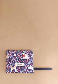 Kompakt tengerészkék virágmintás tasak szarvas- és medveillusztrációkkal, piros masni részlettel és fekete csuklópánttal, bézs h�áttéren.