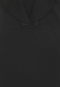 Svart klänning med ett lager av volangdesign vid halsen, som har en liten rosettdetalj. Tillverkad av ett slätt, texturerat tyg.